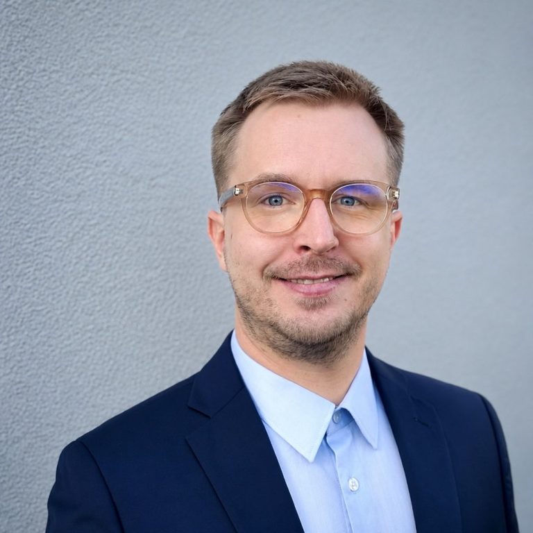Sympathisch lächelnder junger Mann  im blauen Anzug mit Brille, Sebastian Wolz, Bauingenieur, Baubegleitung, -begutachtung