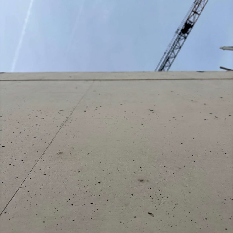 Was ich biete Betongwand mit Blick nach oben, darüber ein Kran, blauer Himmel