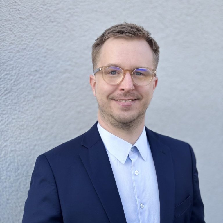 Sebastian Wolz - Bauingenieur Sympathisch lächelnder junger Mann im blauen Anzug mit Brille, Sebastian Wolz, Bauingenieur, Baubegleitung, -begutachtung